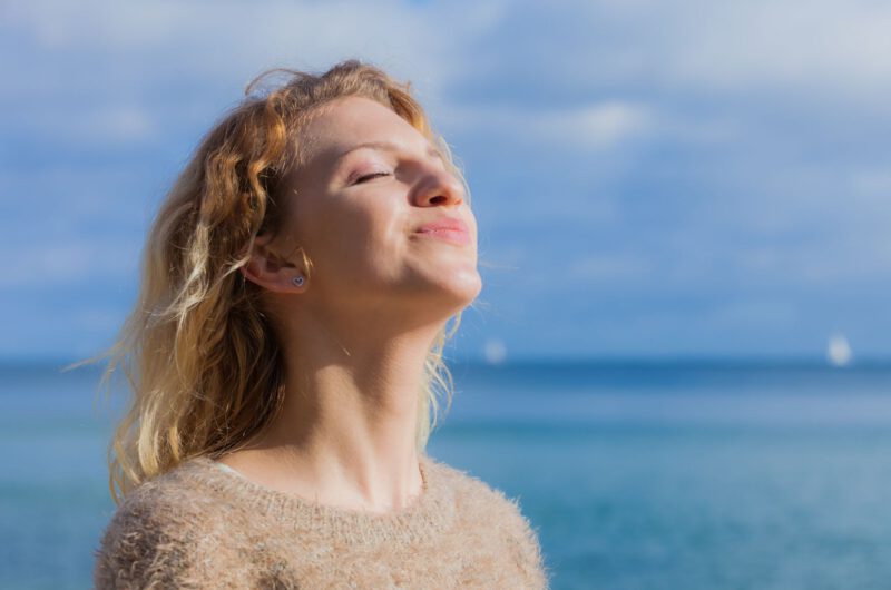 Eine-frau-am-meer-reckt-den-Kopf-mit-geschlossenen-Augen-richtung-Sonne-Ihre-Haut-tankt-vermutlich-Vitamin-D