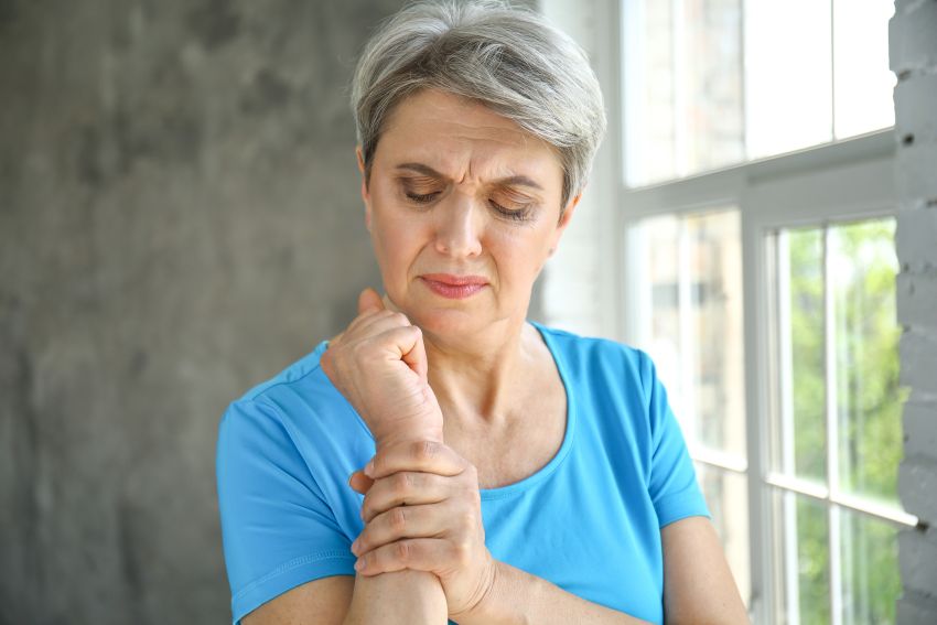 Eine Frau um die 60 hält sich das Handgelenk und hat vermutlich an dieser Stelle Schmerzen von Rheuma oder Athritis