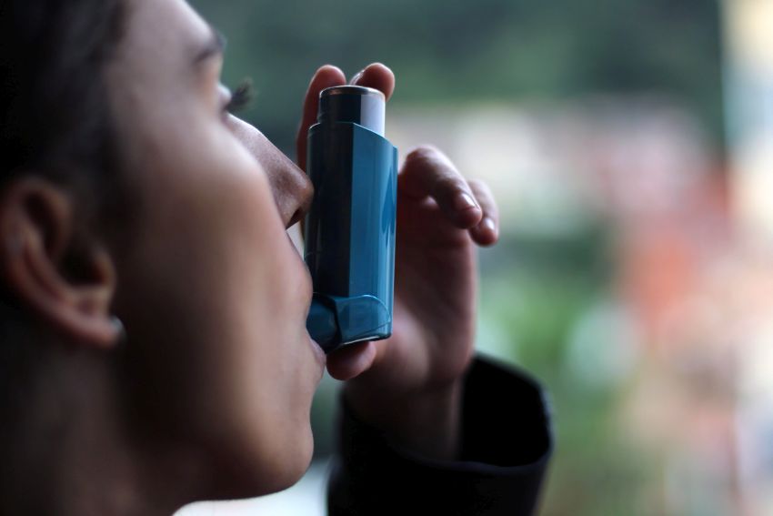 Frau verwendet blauen Asthma-Inhalator, um einen Asthmaanfall zu verhindern. Pharmazeutisches Produkt zur Vorbeugung und Behandlung von Asthma.