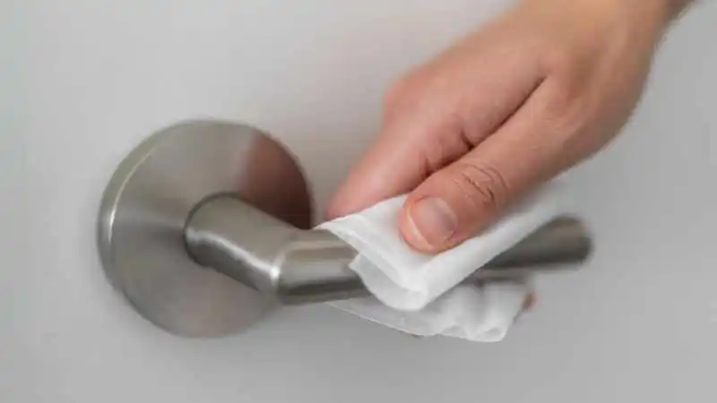Hand an Türgriff an mit Desinfektionstuch