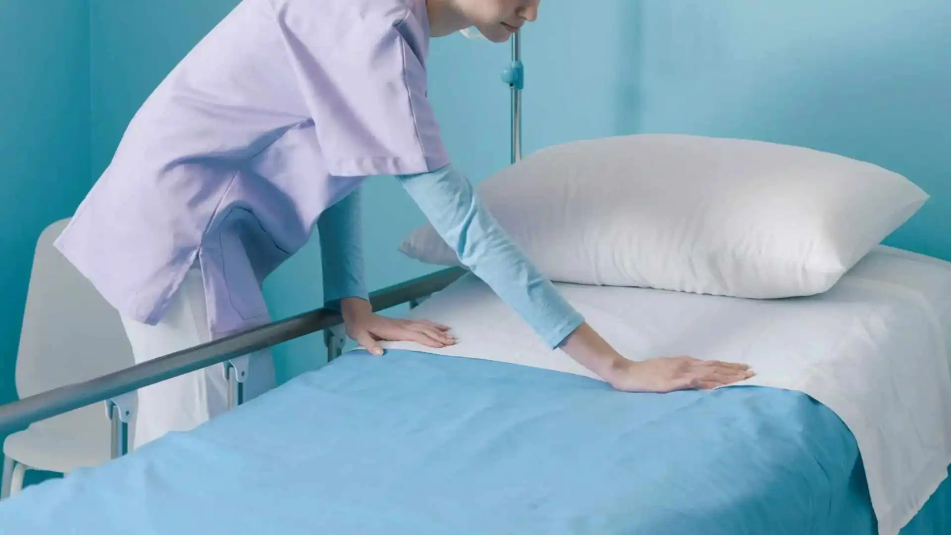 Pflegekraft bereitet Krankenhausbett mit hygienischer Bettauflage und Einmalbettlaken vor